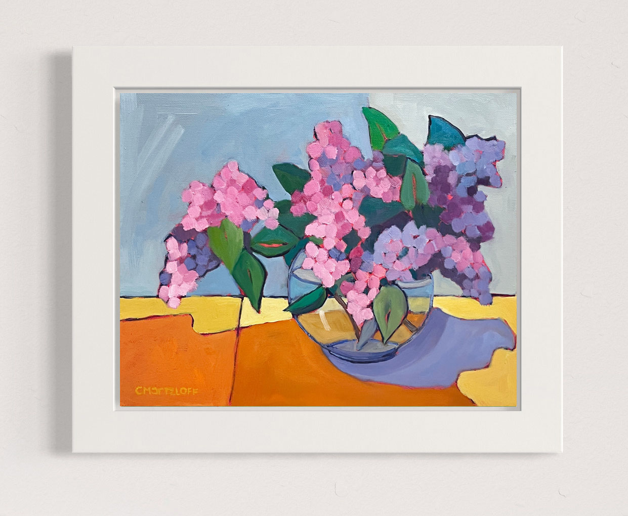 This image captures the expressive beauty of lilacs as a bouquet in a glass bowl of water. Bright pink and violets with touches of green are present. The bouquet gracefully drapes over the sides indicating a sense of relaxed abundance.